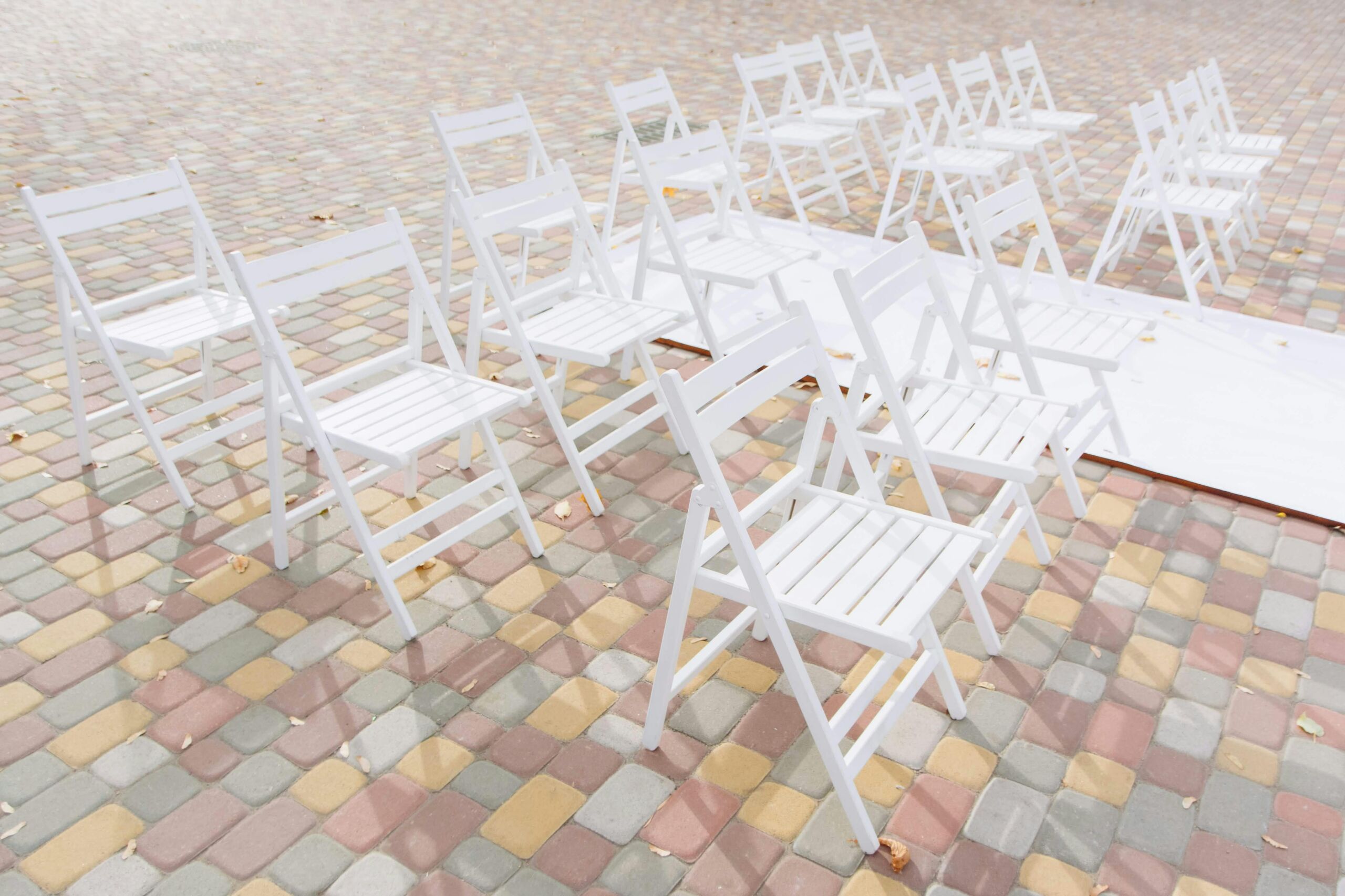 An arrangement of white folding chairs placed on colorful patterned pavers in an outdoor setting.
