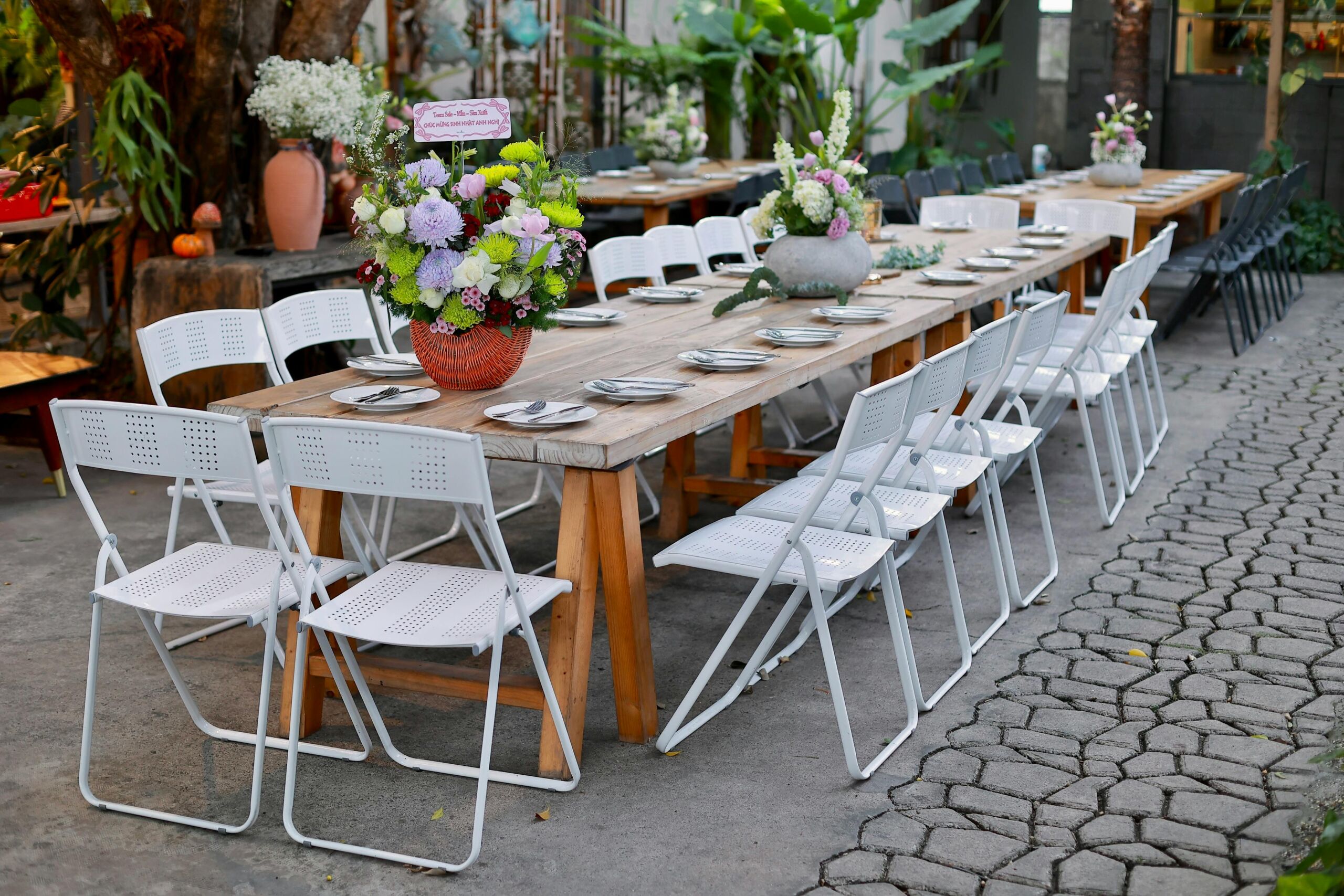 Stylish outdoor dining setup featuring floral centerpieces and white chairs.